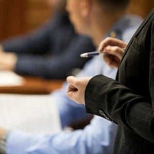 Focused professionals in a formal setting, one in a dark suit with a pen, the other in light blue attire, reviewing documents in an office